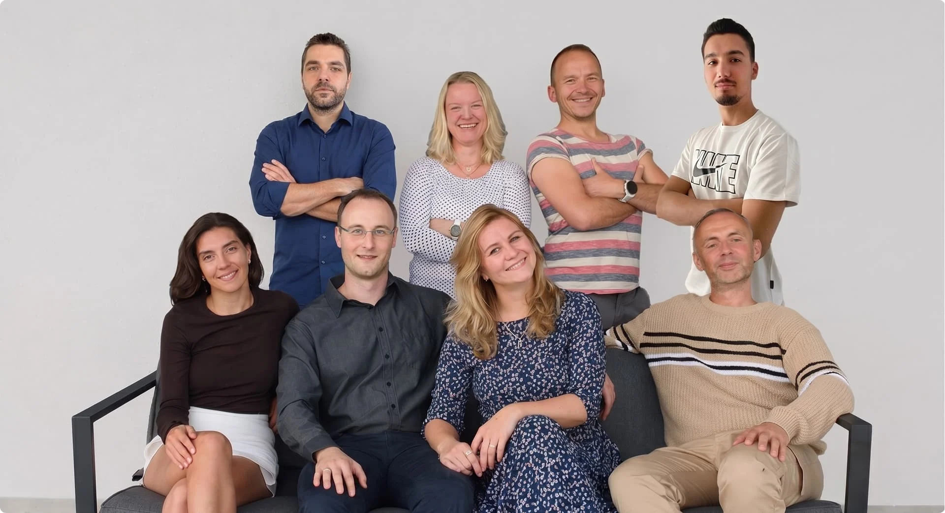 Teamfoto von SEO Revolution mit Mitarbeitenden auf und hinter einer Bank vor heller Wand